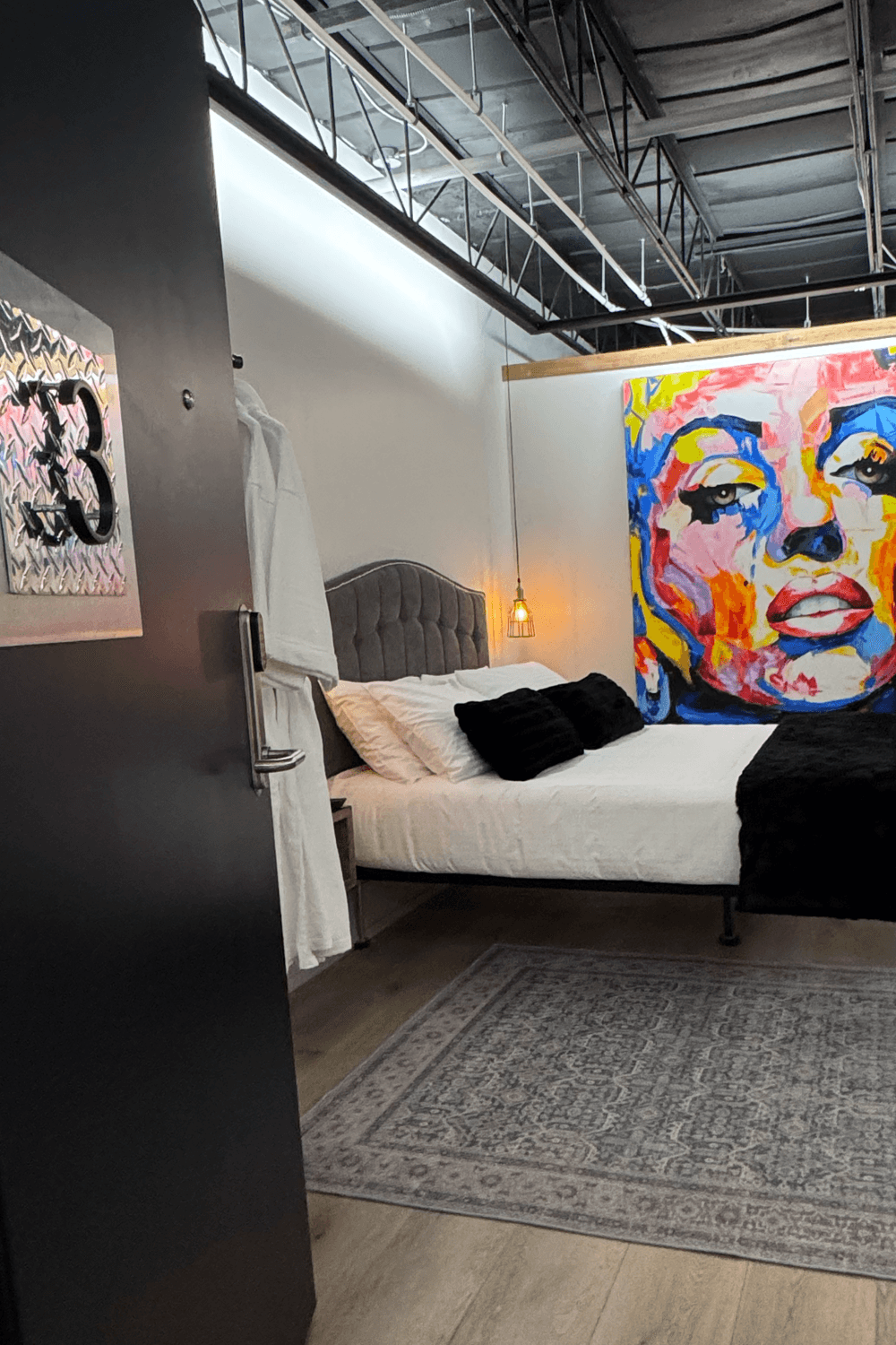 Modern bedroom with an open door labeled "3." A vibrant, large abstract face painting hangs above a bed with white linens and black pillows.