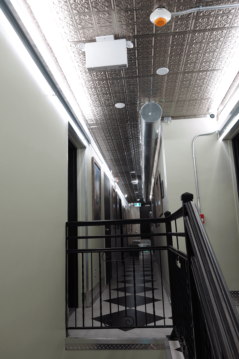 A long hallway with decorative ceiling tiles, lights, and doors lining the walls.